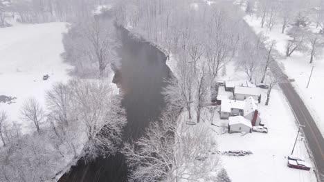 Residential-buildings-near-river-in-small-township-during-blizzard,-aerial-view