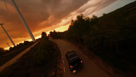 FPV-aerial-drone-view-tracking-a-black-Hummer-driving-along-a-country-highway-at-sunset