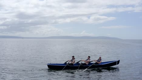 Profile-tracking-side-to-side-drone-follows-currach-rowing-during-the-70th-anniversary-of-currach-racing-in-Galway-bay,-Ireland