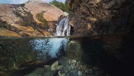 Eine-Malerische-Landschaft-Mit-Einem-Flachen-Fluss-Mit-Felsigen-Ufern,-Kristallklarem-Wasser-Und-Einem-Winzigen-Wasserfall