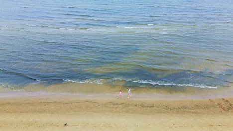 Zwei-Mädchen-Gehen-Und-Tanzen-Am-Leeren-Strand-Neben-Der-Meeresdrohnenantenne