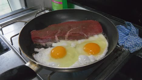 Raw-steak-and-eggs-cooking-in-a-frying-pan-in-a-motorhome-or-campervan