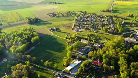 Wide-aerial-view-of-quaint-countryside-village-surrounded-by-large-green-pasture-cropland