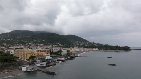 Buildings-on-famous-tourism-island-Ischia-in-Italy,-drone-backward-cloudy-day