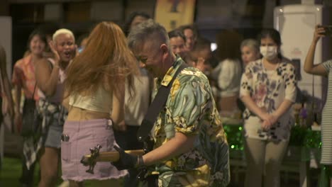 Un-Hombre-Asiático-Toca-El-Bajo-Y-Baila-Junto-Con-Una-Mujer-Asiática-En-La-Pista-De-Baile-Durante-Un-Evento-De-Música-Cultural-étnica-En-Vivo,-Filmado-En-Plano-Medio-En-Cámara-Lenta