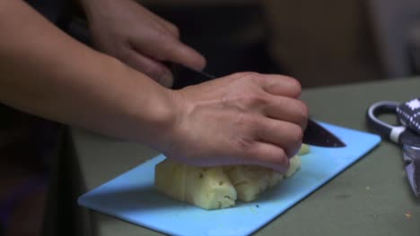 Ananas-Wird-Mit-Einem-Messer-In-Mundgerechte-Stücke-Auf-Einem-Blauen-Schneidebrett-Geschnitten,-Gefilmt-Als-Nahaufnahme