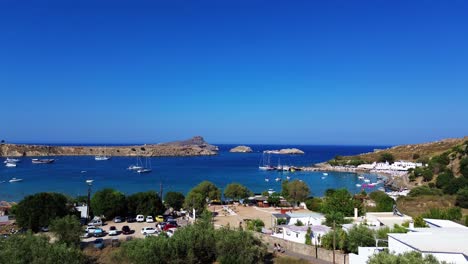 Lindos-beach-and-village-in-Rhodes,-Greece-with-Acropolis-of-Lindos,-houses-and-Mediterranean-sea-during-the-day-filmed-with-the-drone