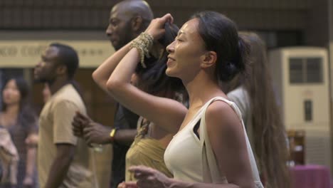 African-man-wearing-black-shirt,-asian-woman-wearing-white-singlet-top,-dancing-at-live-music-event,-filmed-as-medium-close-up-shot-in-slow-motion