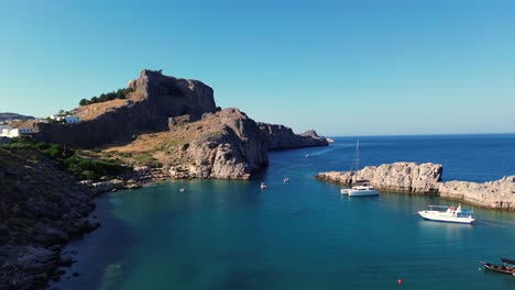 Acropolis-of-Lindos-in-Rhodes,-Greece-with-houses-and-Mediterranean-sea-during-the-day-filmed-with-the-drone