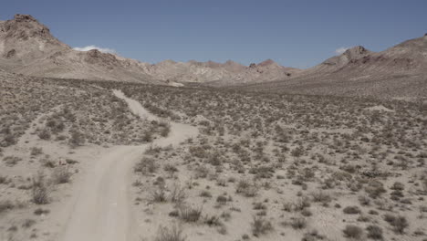 Aerial-flight-through-desert-valley,-4x4-trail-into-the-distance