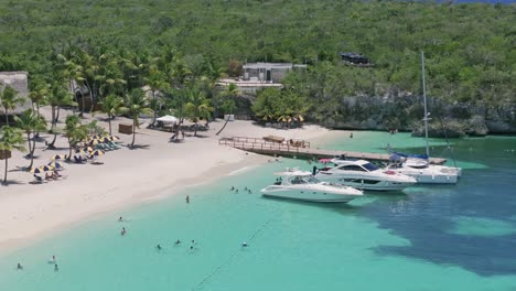 Vista-Aérea-Del-Turista-Descansando-En-El-Claro-Mar-Caribe-Con-Playa-De-Arena-Y-Yates-De-Estacionamiento---Isla-Catalina,-República-Dominicana