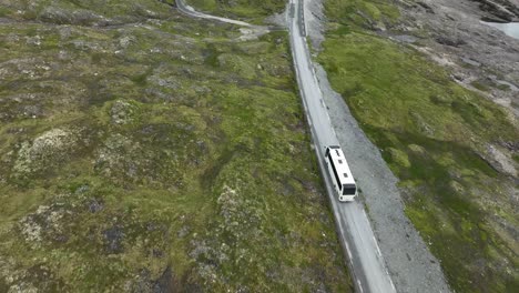 White-sightseeing-bus-driving-tourists-at-Vikafjellet-mountain-pass-in-Norway---Aerial-following-bus-from-above-before-tilt-up-to-reveal-lanscape-towards-Vik-in-Sogn