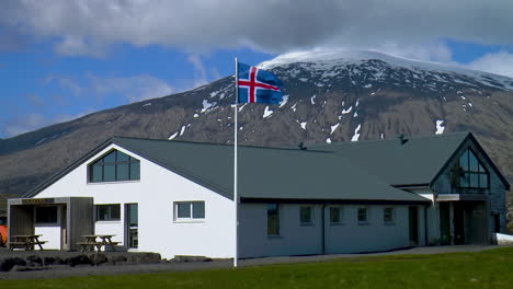 Big,-classic-Icelandic-house-with-Iceland-flag-fluttering-in-the-wind-with-a-view-of-Snaefellsjokull-glacier-and-Stapafell-mountain-in-Iceland-on-Snaefellsnes-peninsula