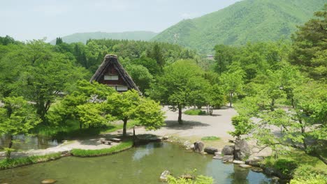 Idyllic-View-Of-Gassho-Thatched-Roof-Surrounded-By-Lush-Green-Foliage-Shirakawago-Beside-Lake