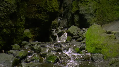 Dark-footage-of-small-river-stream-and-small-waterfalls-inside-cave---Raudfeldsgja-Gorge,-Iceland-on-Snaefellsnes-peninsula