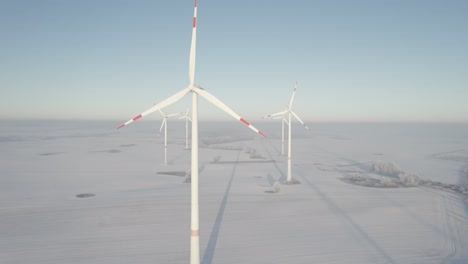 Wind-Turbines-at-sunset-in-snowy-field-near-highway,-aerial-drone-view,-blue-sky