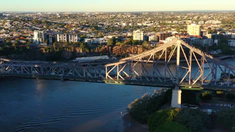 Brisbane-city-aerial-shot,-drone-flyover-and-around-iconic-landmark-Story-bridge-capturing-busy-vehicle-traffics-crossing-the-river-between-Kangaroo-point-and-Fortitude-valley-at-sunset