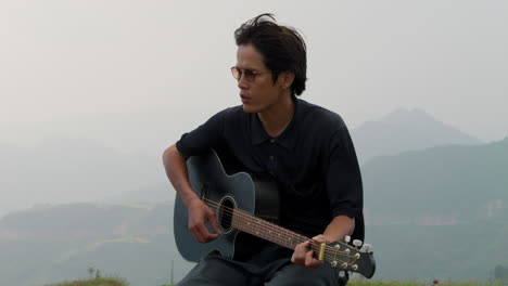 Junger-Thailändischer-Mann,-Der-Einsam-Auf-Einem-Grünen-Berg-Gitarre-Spielt