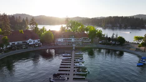 lake-arrowhead-california-village-at-sunset-with-the-sun-beaming-through-the-trees-while-boats-pass-through-the-background-AERIAL-DOLLY-BACK-RAISE-UP