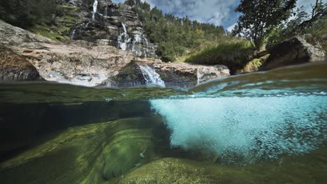 Der-Atemberaubende-Anblick-Der-Felsigen-Ufer-Und-Des-Klaren-Wassers-Eines-Flachen-Flusses-Sowie-Eines-Malerischen-Wasserfalls