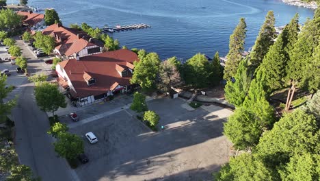 pass-over-lake-arrowhead-village-in-california-revealing-the-bright-blue-lake-and-marina-dockside-AERIAL-DOLLY-TILT-UP-4K