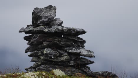 A-cairn-made-of-dark-jagged-stones-on-a-moss-covered-rocky-terrain
