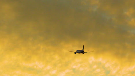 Airplane-During-Flight-Flying-Against-Bright-Orange-Sky-At-Dusk
