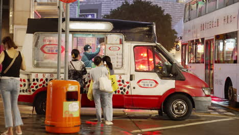 Women-standing-on-the-side-of-the-road-buying-ice-cream-from-a-car-stall-at-night-in-the-city-of-Hong-Kong,-China