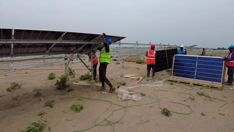 Gruppe-Von-Männern-Mit-Ingenieuren-Und-Technikern,-Die-Photovoltaikmodule-Bei-Einem-Solarparkprojekt-In-Jambur,-Gambia,-Westafrika,-Installieren