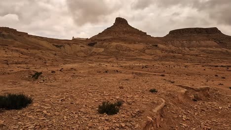 Driving-along-desert-road-with-Ksar-Guermessa-troglodyte-village-in-background-in-Tunisia-on-cloudy-day