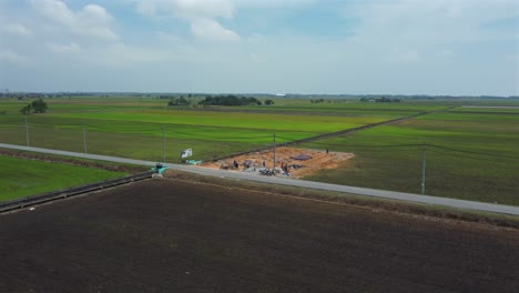 Construction-work-going-on-near-green-paddy-fields,-aerial-point-of-interest-shot