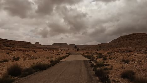 Driving-on-desert-road-in-Tunisia-with-Ksar-Guermessa-troglodyte-village-in-background-cloudy-day