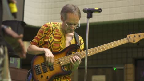 Male-caucasian-playing-5-string-electric-bass-guitar-on-stage-during-live-music-performance,-filmed-as-medium-shot-in-slow-motion-handheld-style
