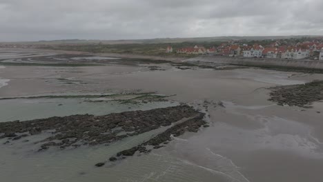 Drone-flying-away-from-the-small-coastal-village-Ambleteuse-during-a-stormy-summer-day-during-low-tide
