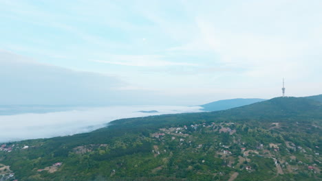 Sobre-La-Niebla,-Pecs,-Hungría,-Mañana,-Montaña-Con-Una-Torre-Al-Fondo,-Pueblo-Al-Amanecer,-Cielo-Nublado