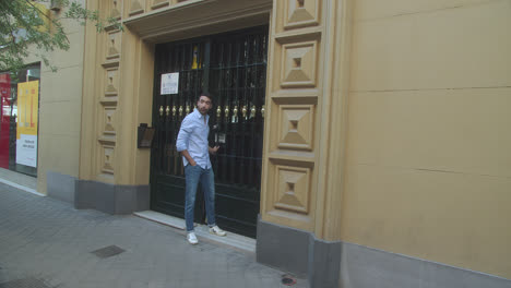 Wunderschöne-Zeitlupenaufnahme-Eines-Jungen-Lateinamerikanischen-Mannes,-Der-Nachmittags-Ein-Gebäude-Verlässt,-Um-Eine-Straße-In-Madrid-Entlang-Zu-Gehen