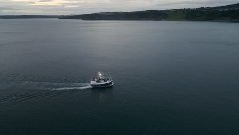 Drohnenaufnahme-Eines-Fischerbootes,-Das-Im-Morgengrauen-Landeinwärts-In-Richtung-Scarborough-Fährt,-Mit-Hellen-Lichtern