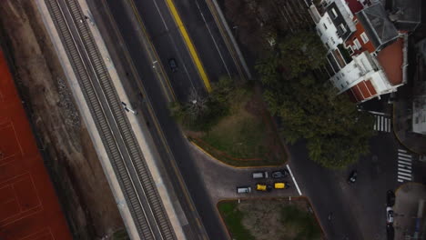 The-camera-is-circling-over-the-highway-in-Buenos-Aires,-cars-drive-along-the-road,-next-to-the-railway