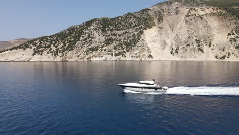 White-luxurious-boat-drives-along-Greek-coastline,-aerial-backward-establisher