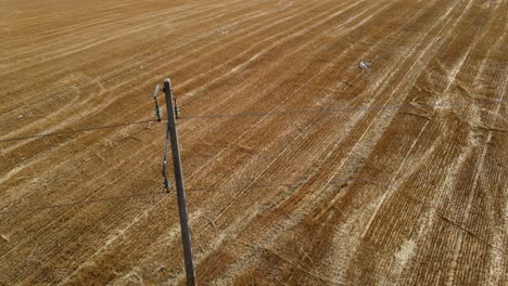 Sideview-of-concrete-utility-pole-held-up-above-farm-fields,-drone