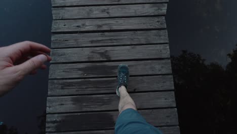 Looking-down-POV-of-man-walking-to-edge-of-pier-dock-wooden-boards-and-looking-into-alpine-lake