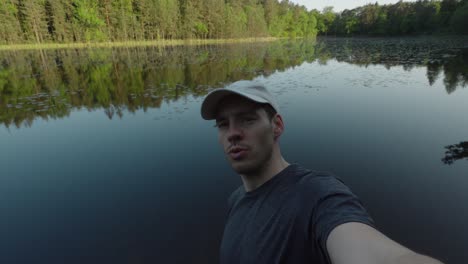 Man-shows-off-clear-reflection-on-lake,-view-of-forest-outside-in-the-shade,-selfie-POV
