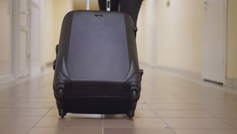 Woman-carries-big-black-suitcase-on-tile-floor-of-corridor