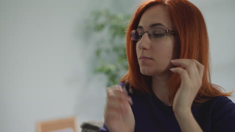 Woman-with-ginger-hair-puts-on-glasses-to-continue-work