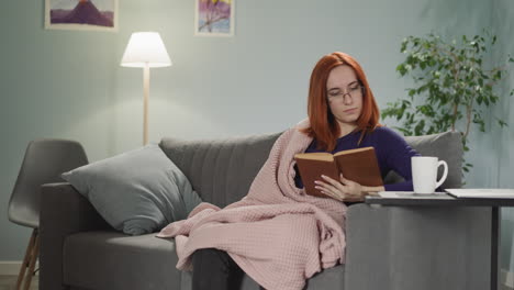 Redhead-woman-reads-interesting-book-sitting-on-sofa