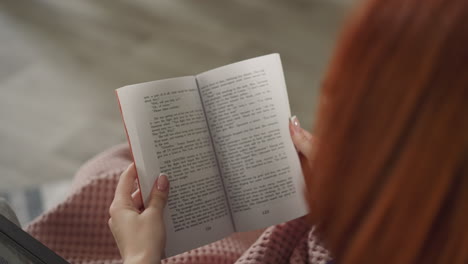 Redhead-woman-flips-book-pages-reading-story-in-English