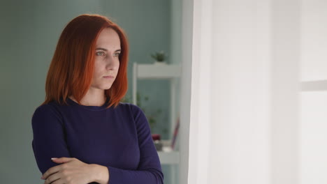 Depressed-woman-with-ginger-hair-looks-out-bright-window
