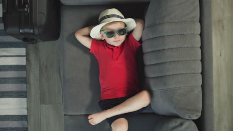 Relaxed-toddler-in-sunglasses-and-hat-enjoys-lying-on-sofa