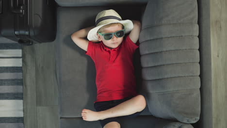 Little-boy-in-straw-hat-relaxes-on-couch-moving-with-foot