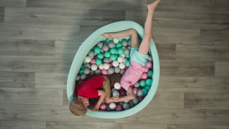Positive-boy-and-girl-crawl-among-plastic-balls-in-dry-pool